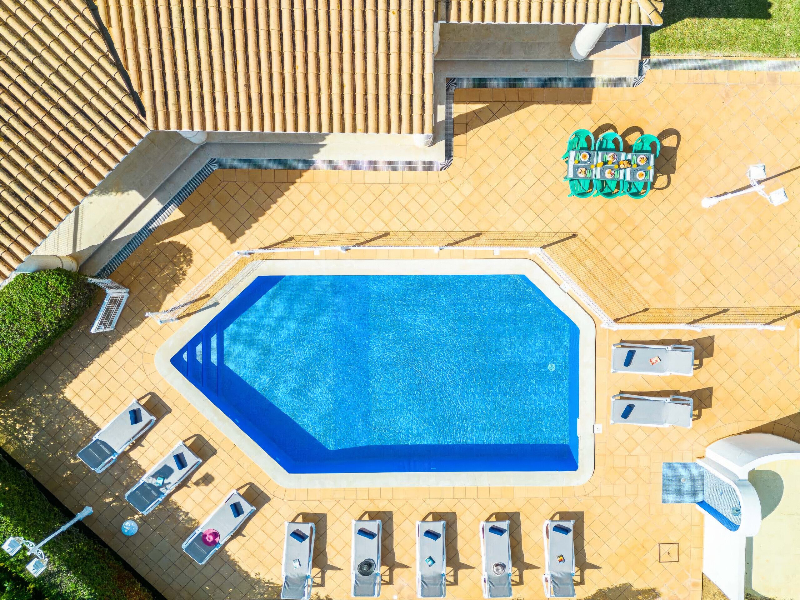 An aerial view of a swimming pool with sun loungers and a small table with drinks.