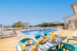 A poolside dining area with a table set for breakfast, overlooking a swimming pool.