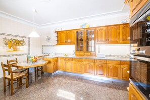 A kitchen with wooden cabinets, a granite countertop, and a dining area with chairs and a table. - Family retreat w/ heatable pool & BBQ (Albufeira)