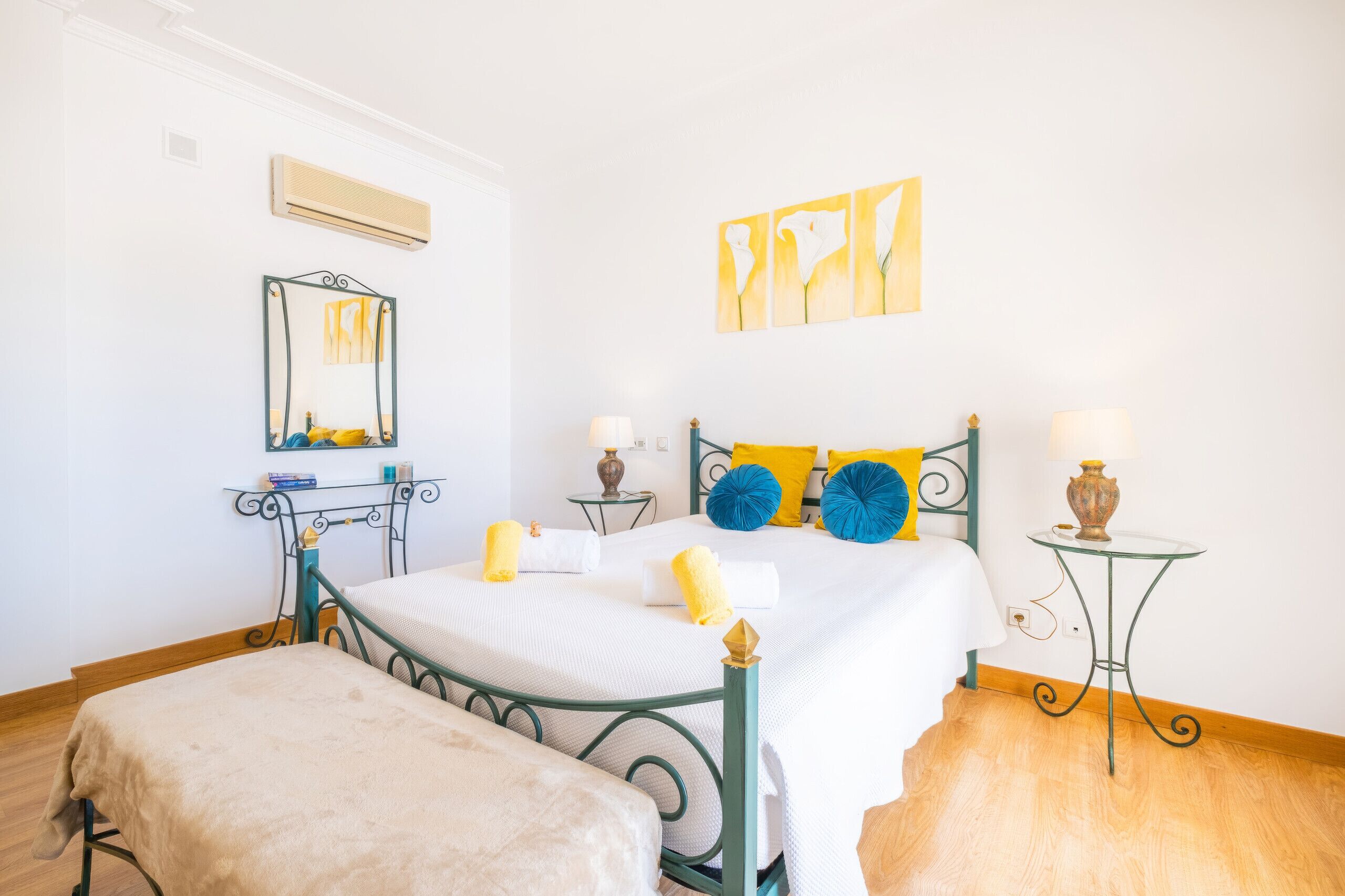 Un dormitorio con cama, mesita de noche, espejo y cuadros en la pared.