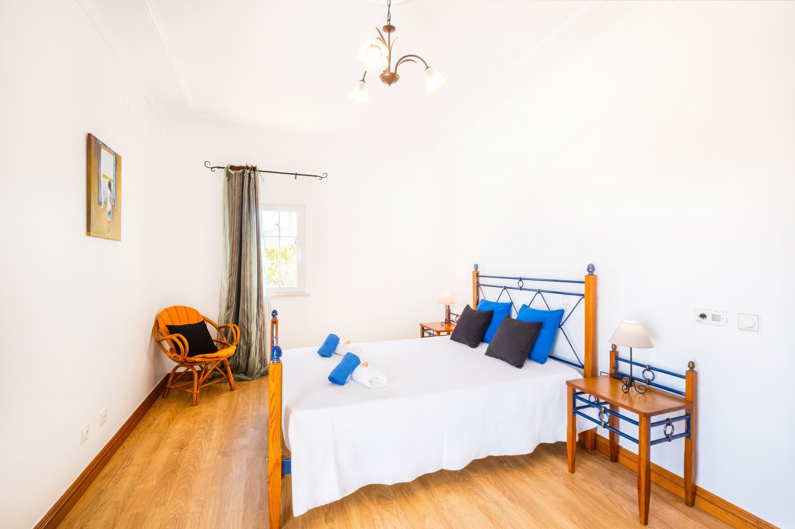 Un dormitorio con cama, una silla, una mesita de noche, una lámpara y un cuadro en la pared.