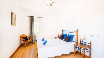 Un dormitorio con cama, una silla, una mesita de noche, una lámpara y un cuadro en la pared.
