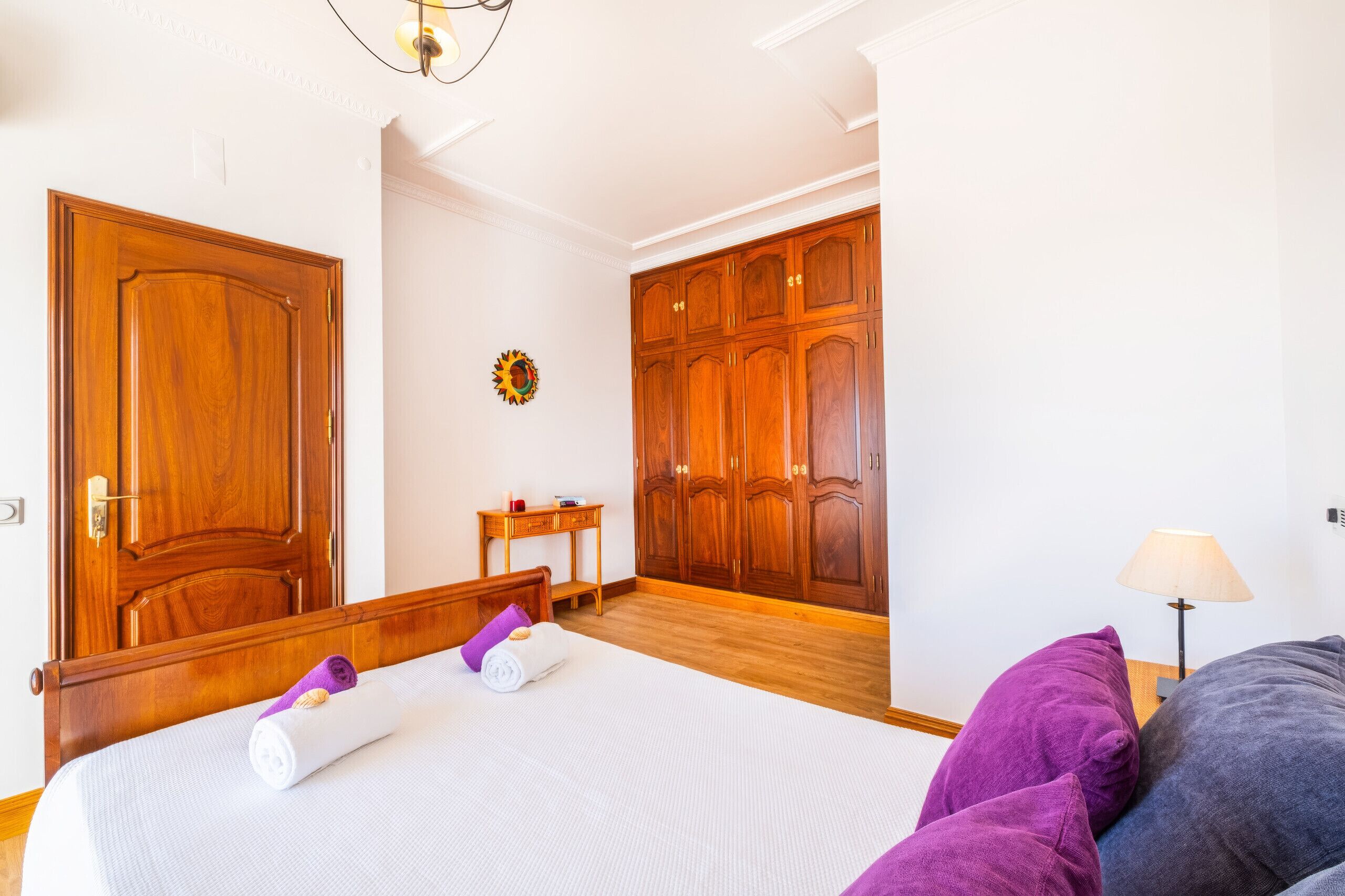 A hotel room with a wooden bed, a small bedside table, a wardrobe, and a lamp.