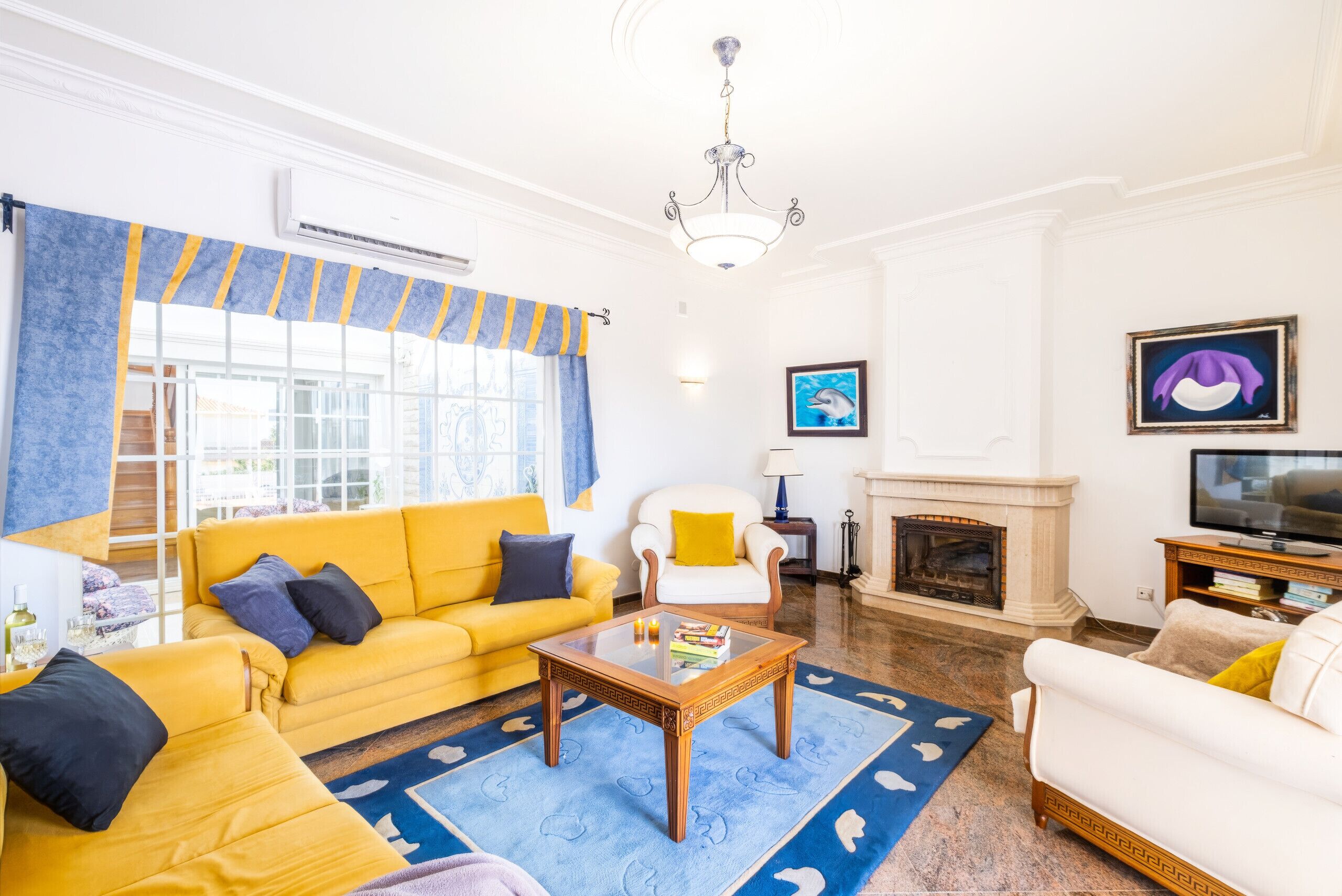 A living room with a yellow sofa, a white armchair, a fireplace, and a television.