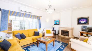 A living room with a yellow sofa, a white armchair, a fireplace, and a television.