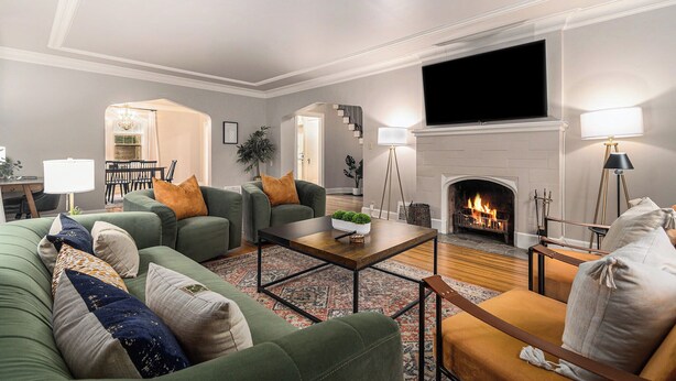A living room with green sofas, a coffee table, a fireplace, and a TV. - Dundee's 3BR Upscale Retreat, Near Downtown! (Omaha)