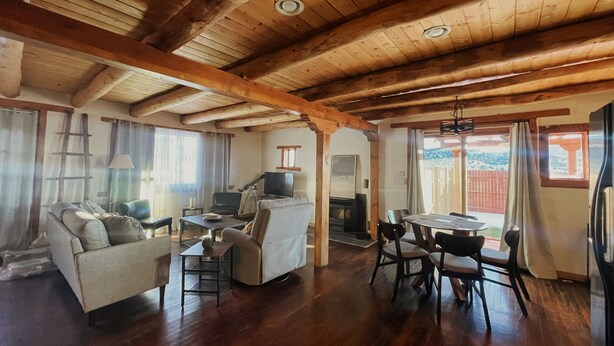 A spacious living area with wooden beams, a fireplace, a sofa, a dining table, and chairs. - Cantina Stagecoach Stop (Grants)