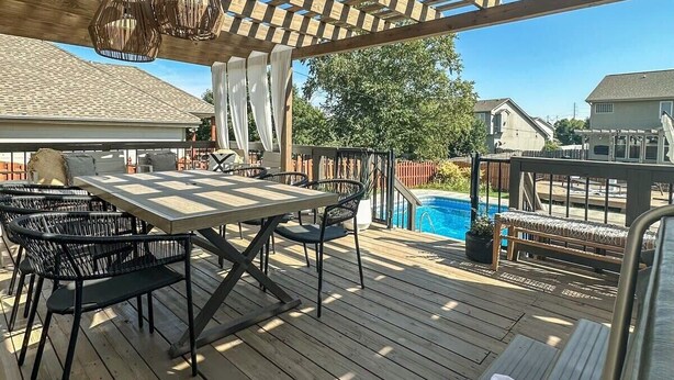 Eine Holzterrasse mit einer Pergola, Sitzgelegenheiten im Freien und einem Pool.