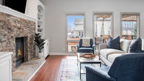 Ein Wohnzimmer mit Kamin aus Stein, einer Couch, einem Couchtisch und Blick ins Freie.
