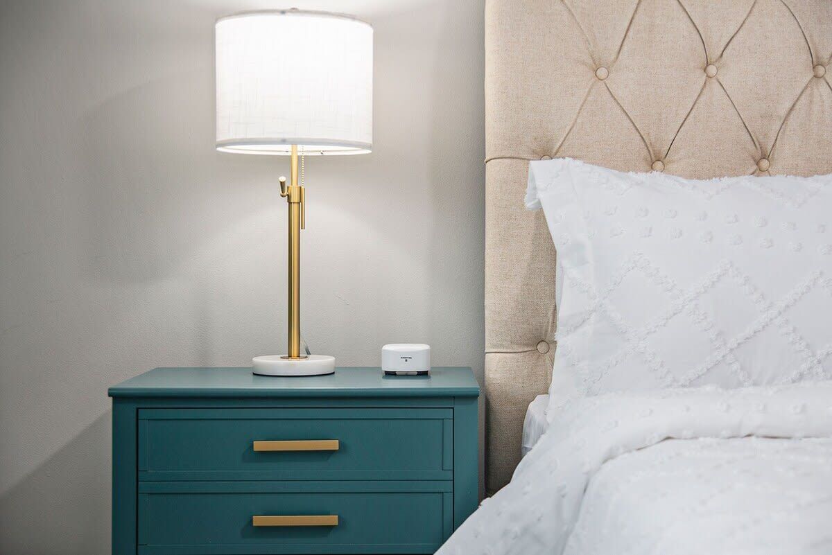 A teal bedside table with a gold lamp, a white bedside table lamp, and a white bedside device.
