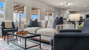 Ein geräumiges Wohnzimmer mit einem beigen Sofa, dunklen Sesseln und einem Glastisch.