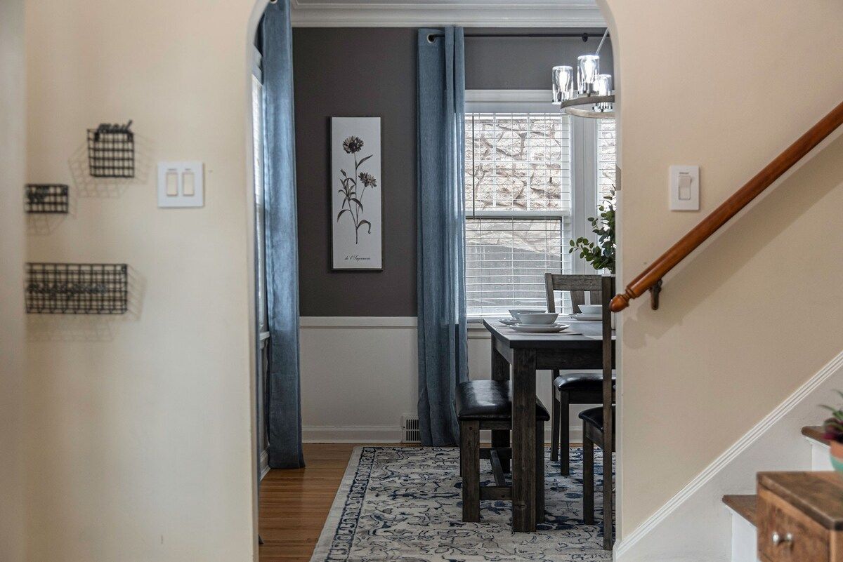 A hallway with a dining area, a staircase, and a window with curtains.