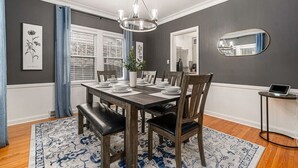 Een eetkamer met een houten tafel gedekt voor vier personen, een kroonluchter en een spiegel aan de muur.