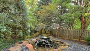 Een tuin met een kleine waterval, omringd door rotsen en diverse planten.