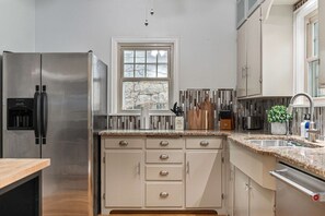 A modern kitchen with a stainless steel refrigerator, white cabinetry, a window above the sink, and a granite countertop.