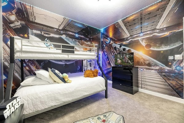 Ein Schlafzimmer im Stil von Star Wars mit einem Etagenbett, einem Fernseher und Wandbildern zum Thema Weltraum.