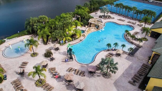 A pool area with lounge chairs, palm trees, and a tennis court. - 5 BR Villa+Pool&Lake views+Near Disney+WaterPark (Kissimmee)