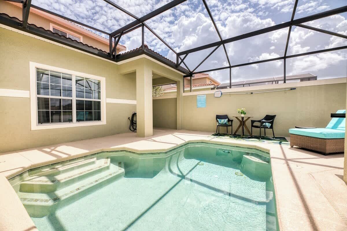A swimming pool with steps, a covered patio, and outdoor seating.