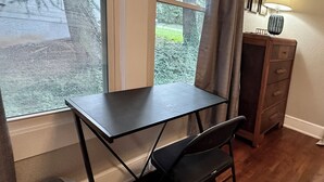 A small room with a desk, chair, and a lamp. There is a window with curtains, a trash can, and a dresser with a lamp on top. - Extended Stay NE Hickory 1 Bedroom 1 Bath Workspace, Washer Dryer, duplex apt. (Hickory)