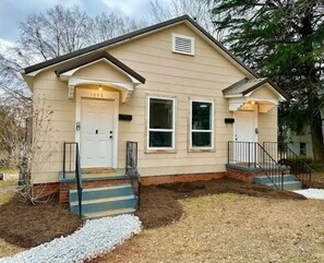 Welcome to a charming single-story residence with a front door, two windows, and a beautifully manicured lawn.