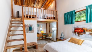 A bedroom with a bunk bed, wooden staircase, a desk with a lamp, a chair, and a bed with a quilt and pillows.