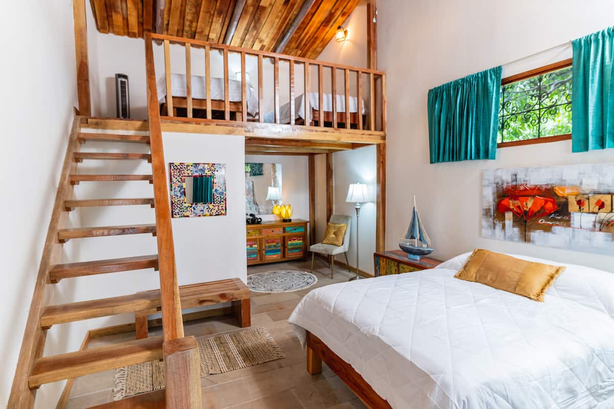 Ein Schlafzimmer mit Etagenbett, einer Holztreppe, einem Schreibtisch mit Lampe, einem Stuhl und einem Bett mit Tagesdecke und Kissen.