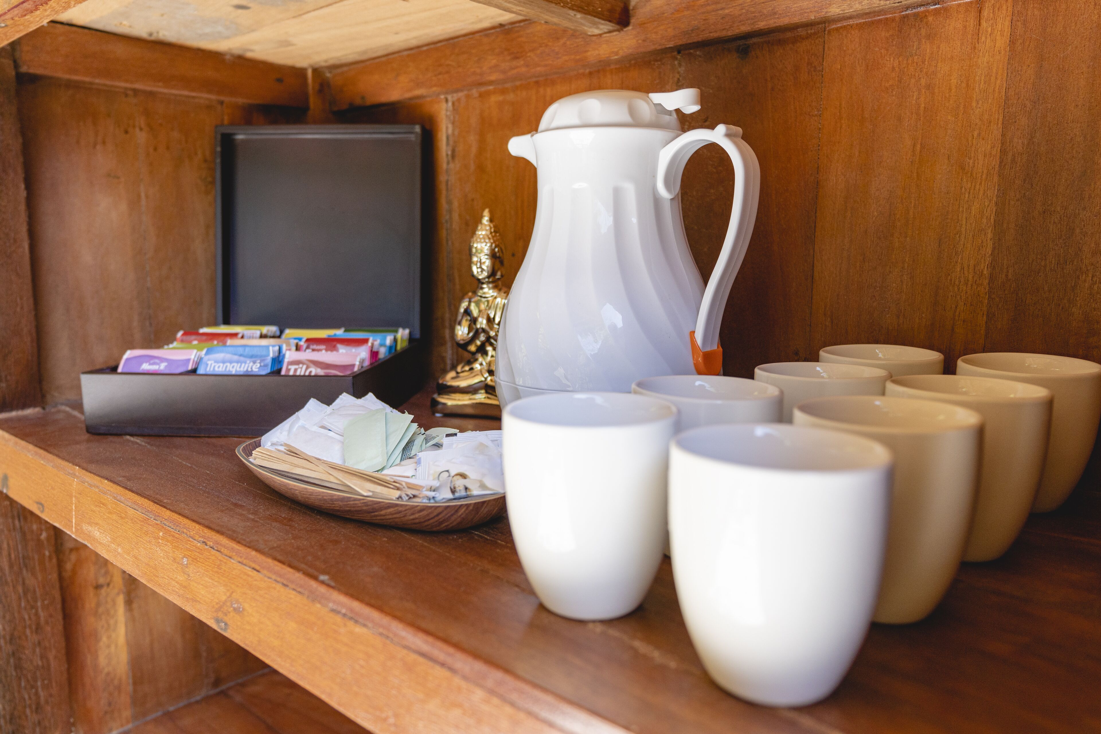 A wooden counter with a white pitcher, several white cups, a basket of papers, and a television.
