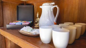 A wooden counter with a white pitcher, several white cups, a basket of papers, and a television.