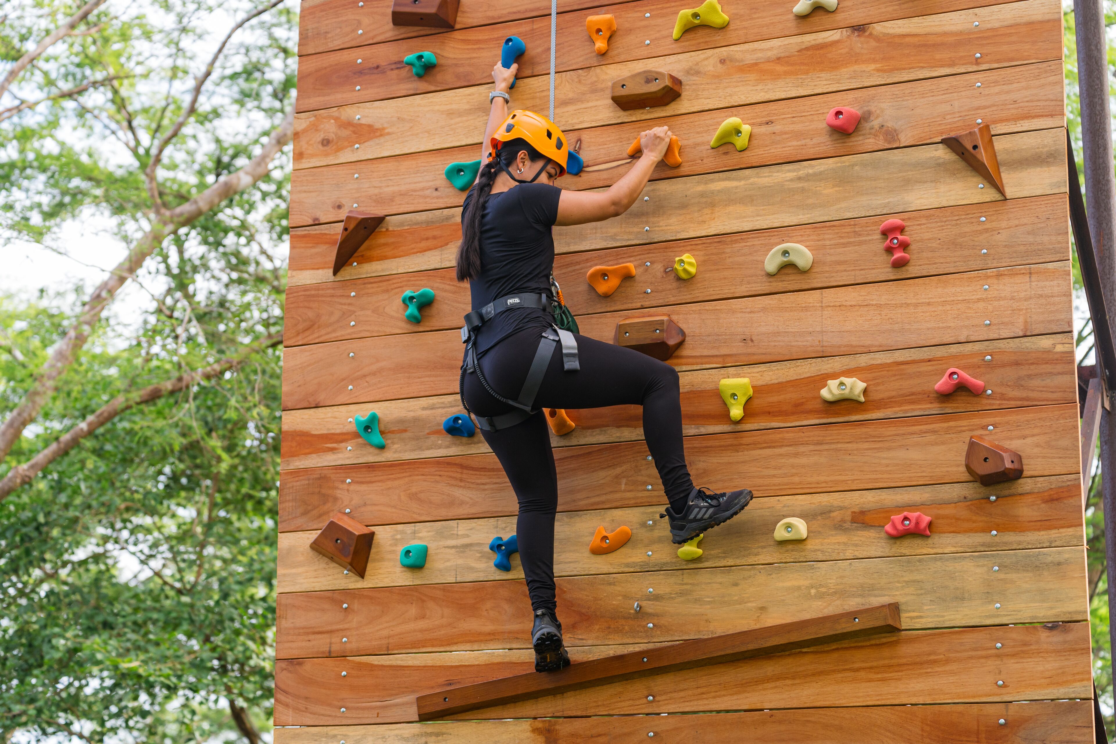 Una persona escalando una pared de madera con puntos de agarre de distintos colores.