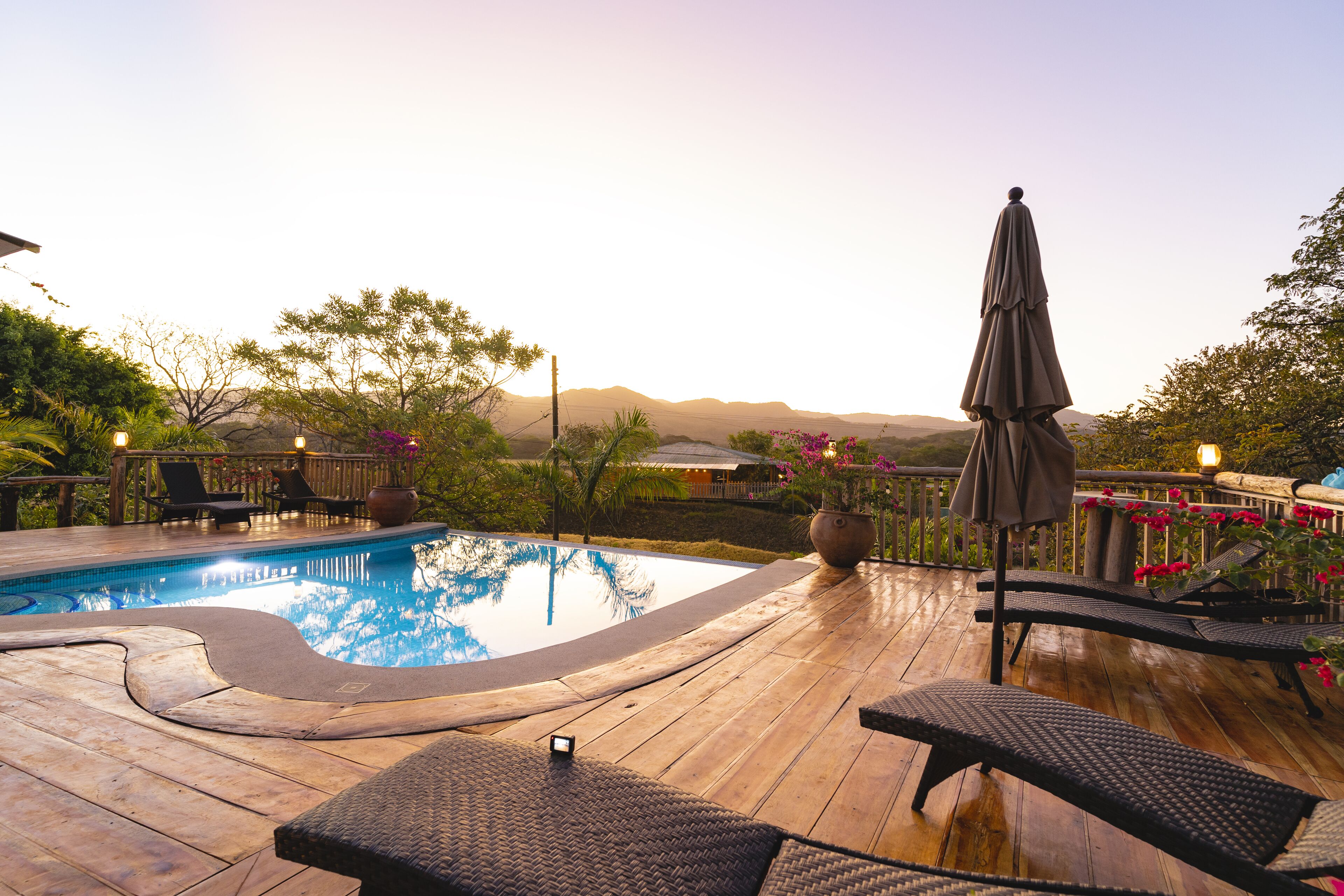 A wooden deck with a swimming pool, lounge chairs, and a view of distant mountains.