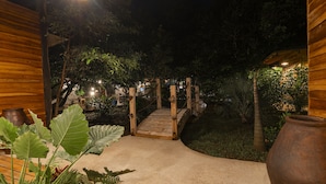 A wooden bridge leading to a garden area with potted plants and a large pot.