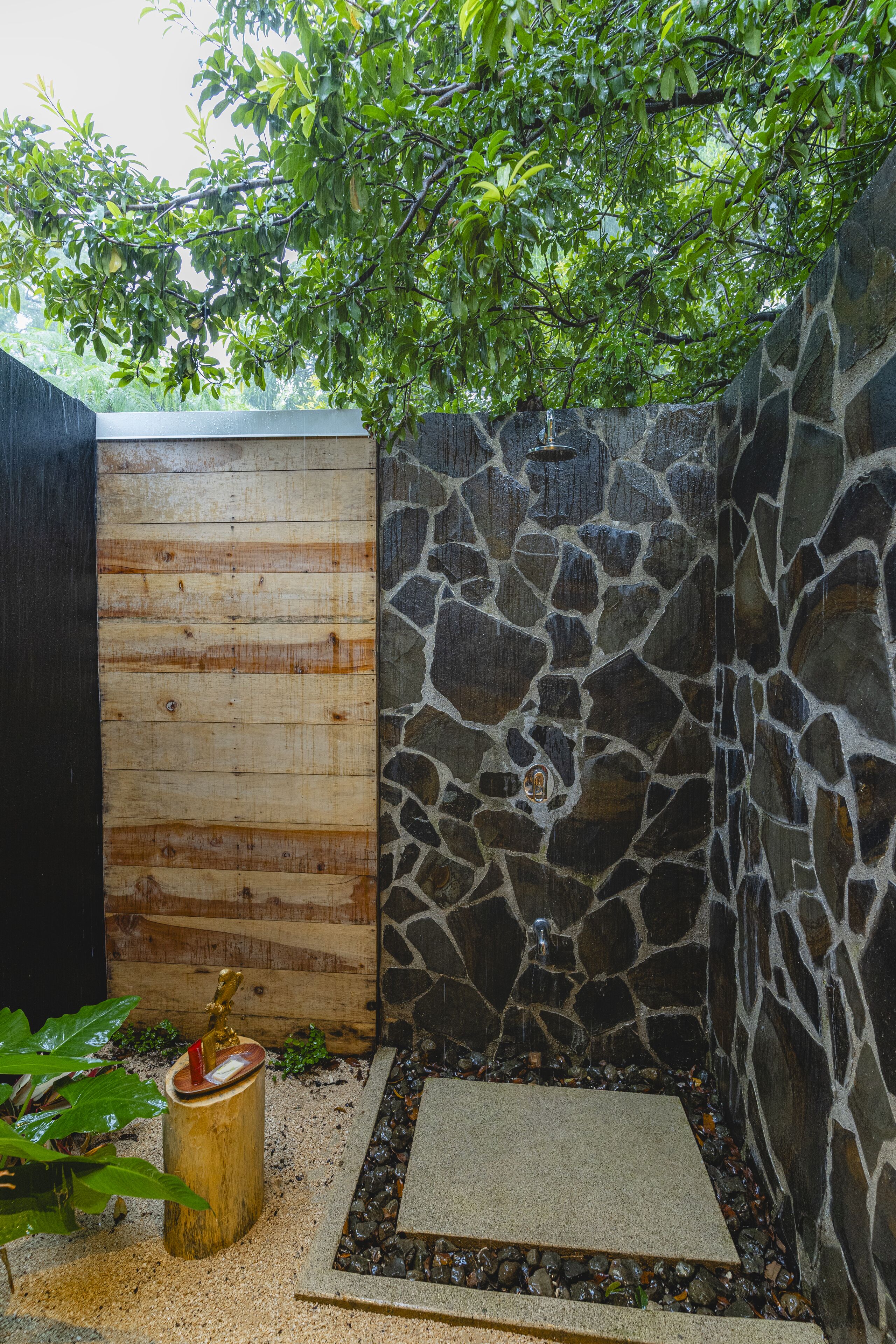 A stone-walled shower area with a wooden bench and a small plant.