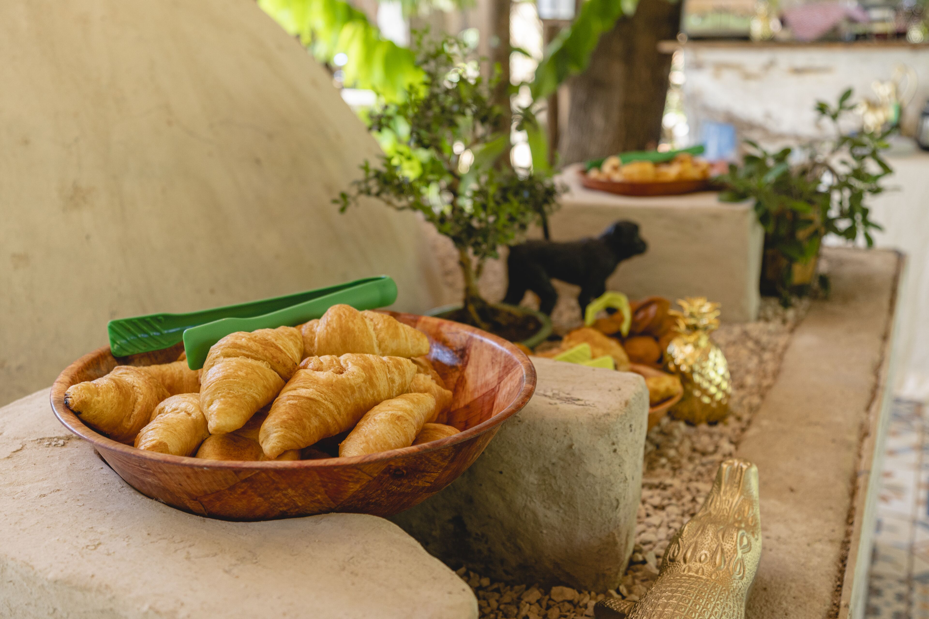 A wooden bowl filled with croissants on a stone surface, surrounded by decorative items and a small tree.