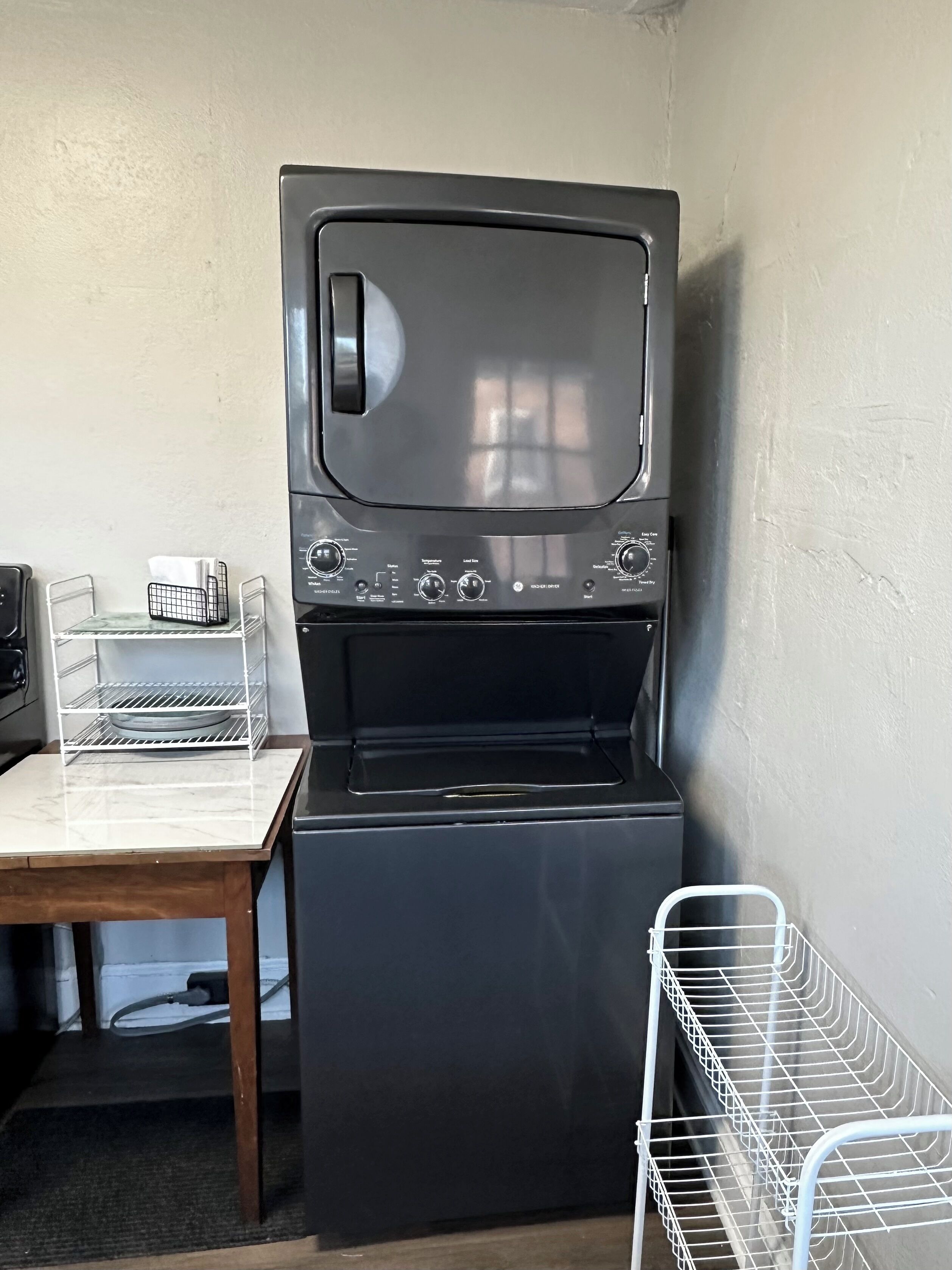 Un appareil compact, de couleur sombre, combinant une machine à laver et un sèche-linge, doté d’un panneau de commande avec plusieurs boutons et molettes.
