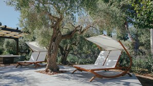 Outdoor seating with white canopies and wooden frames, set against a backdrop of trees and a pergola. - Archi Bianchi  (Cefalù)
