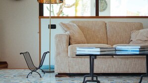 A room with a patterned floor, a beige sofa with a book on it, and a metal chair. - Archi Bianchi  (Cefalù)