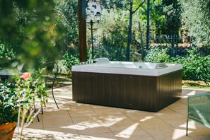 Un jacuzzi en un entorno exterior, con suelo de baldosas y vegetación circundante.