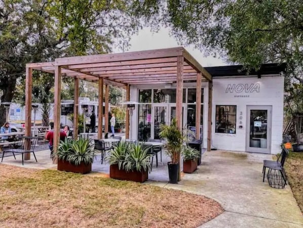 Relax in a serene outdoor setting surrounded by lush greenery and potted plants, with a nearby coffee shop just steps away.