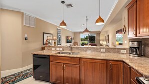 A modern kitchen with granite countertops, wooden cabinets, a dishwasher, and pendant lighting.