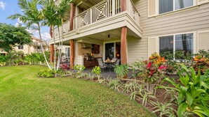 A two-story house with a covered patio, outdoor furniture, and a variety of tropical plants.