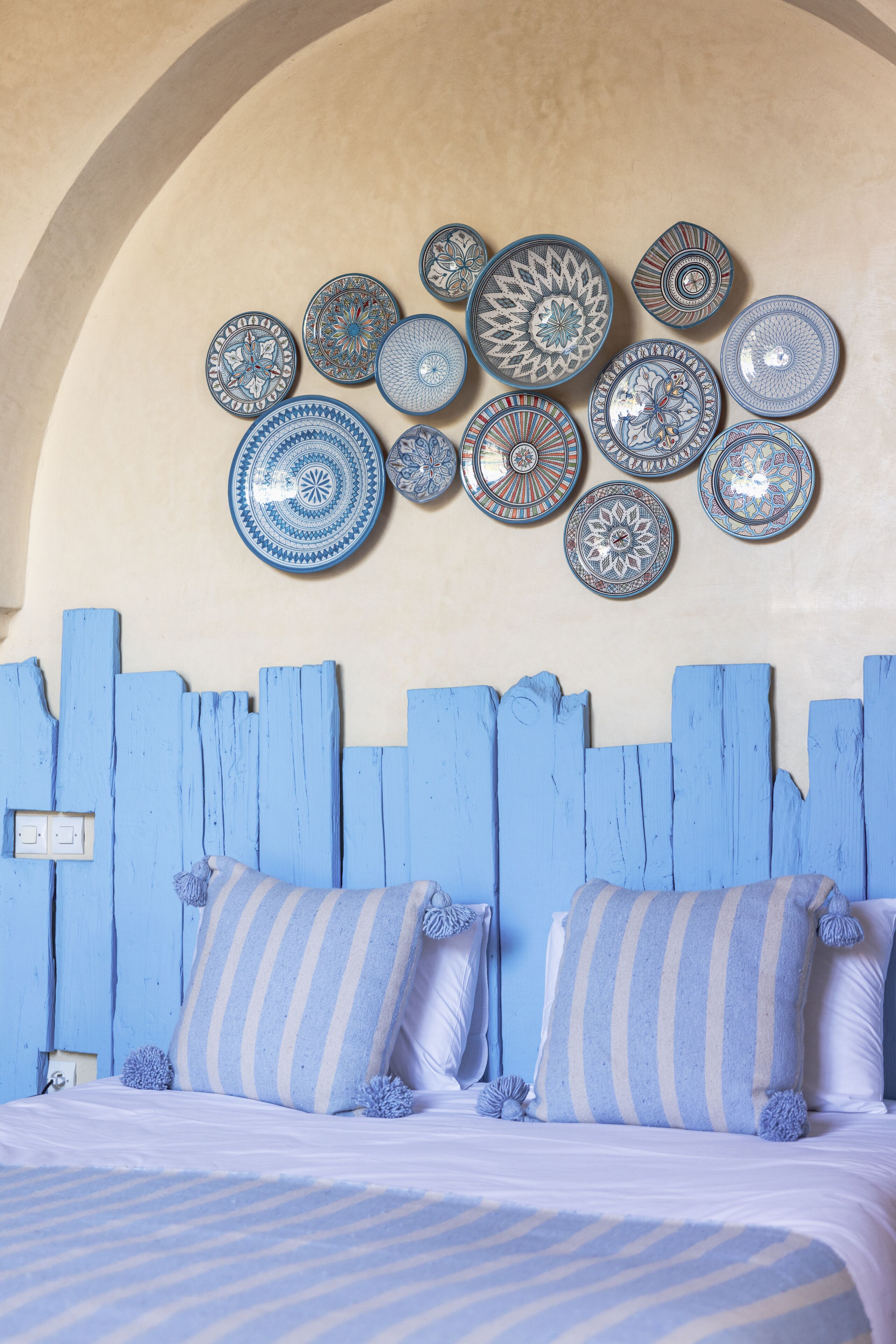 A bedroom with a blue-painted headboard, a bed with striped bedding, and a collection of decorative plates on the wall.