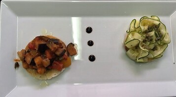 Une assiette rectangulaire blanche contenant deux plats : un mélange de légumes et de viande à gauche, et une salade de concombres à droite, avec trois points noirs au centre.