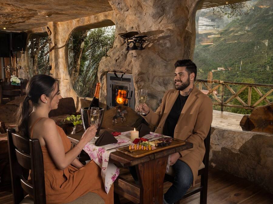 Un comedor rústico con pared de piedra, chimenea y vista panorámica de un paisaje montañoso.