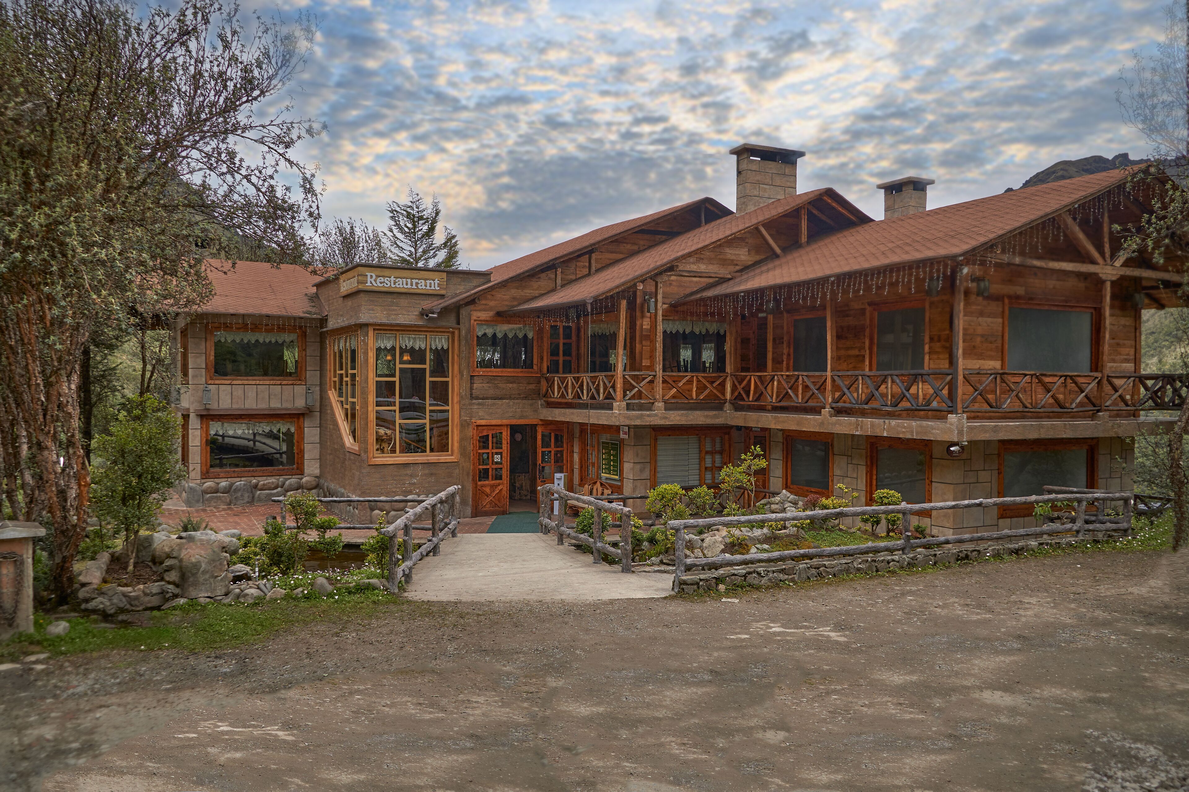 Un bâtiment rustique en bois, avec une enseigne indiquant « Restaurant », un balcon et un chemin de pierre menant à l’entrée.