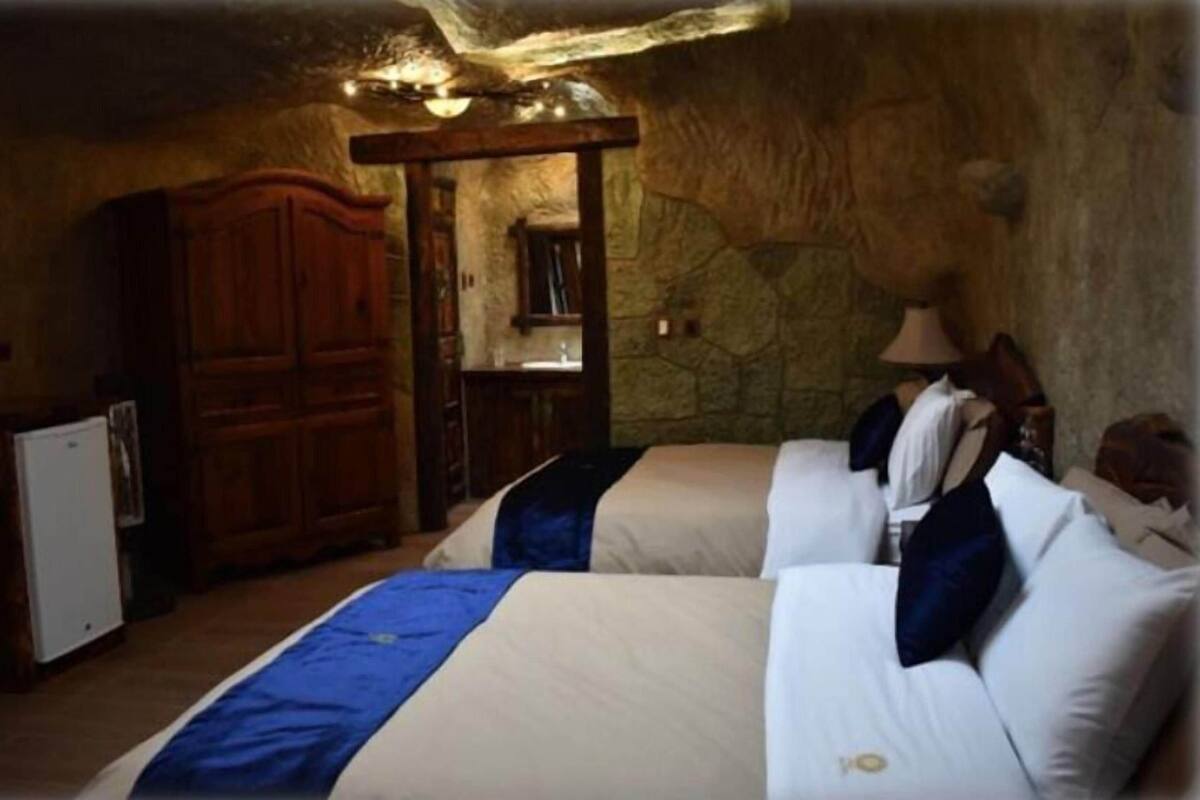 Une chambre avec deux lits, une armoire en bois, des murs en pierre et une petite table avec une lampe.