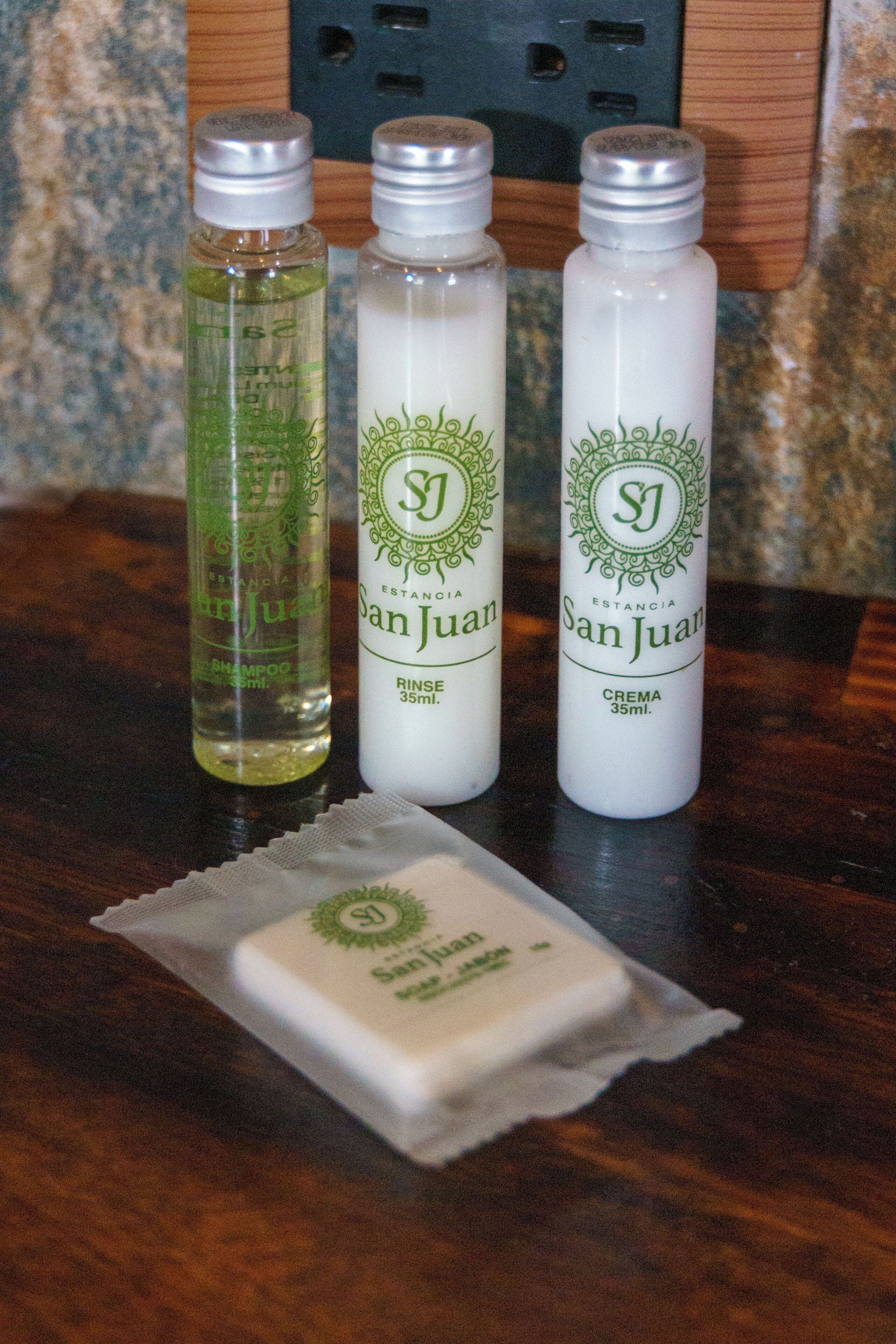 Tres botellas de productos para el cuidado del cabello San Juan sobre una superficie de madera.