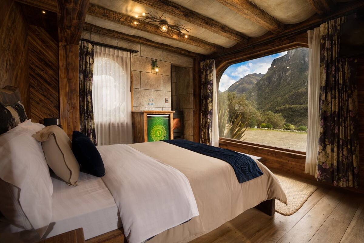 Une chambre dotée d’un grand lit, de murs en bois, d’une cheminée en pierre et offrant une vue sur les montagnes.