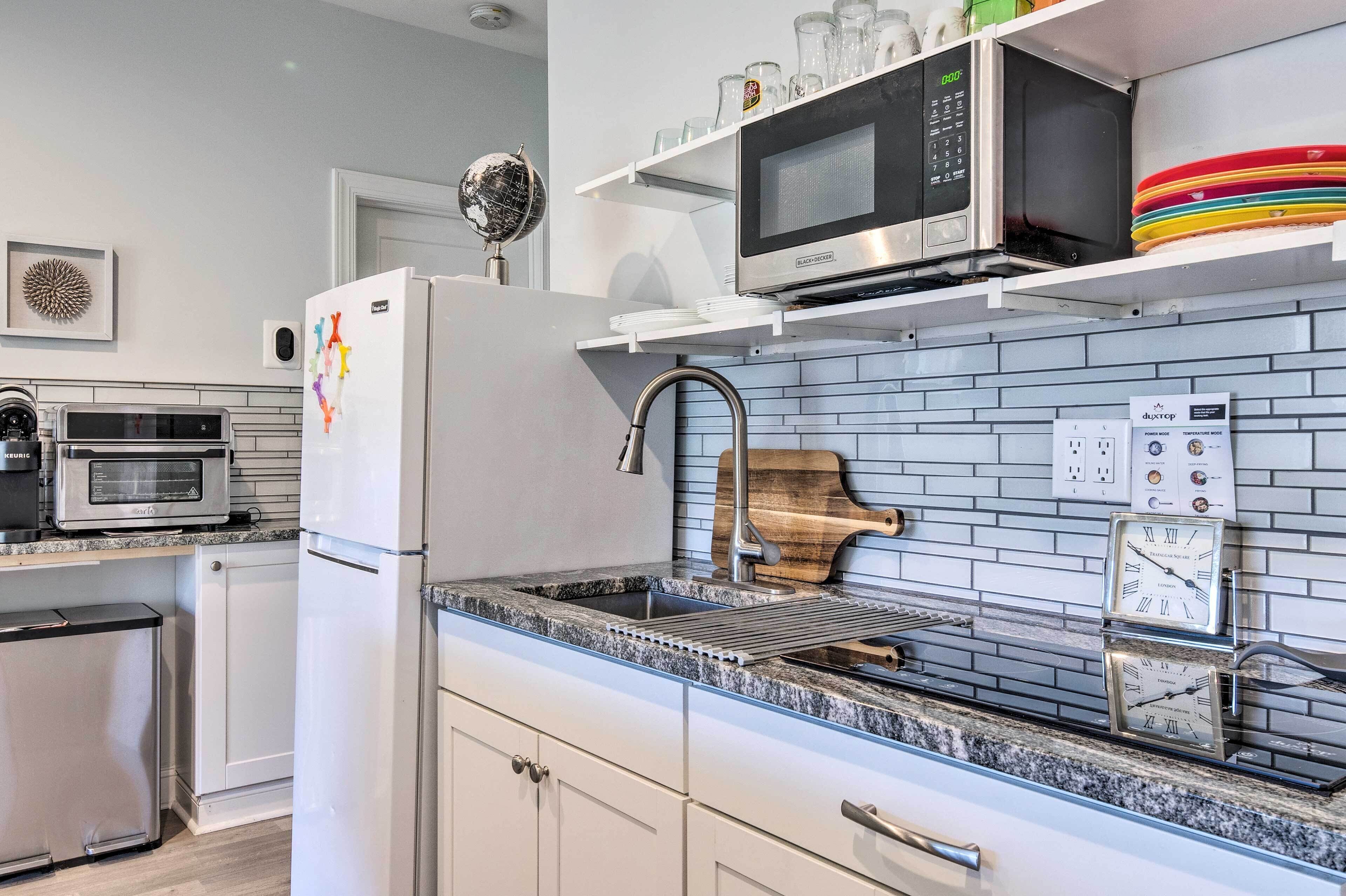 A modern kitchen with a built-in microwave, a stainless steel refrigerator, a sink with a wooden cutting board, and a clock on the wall.