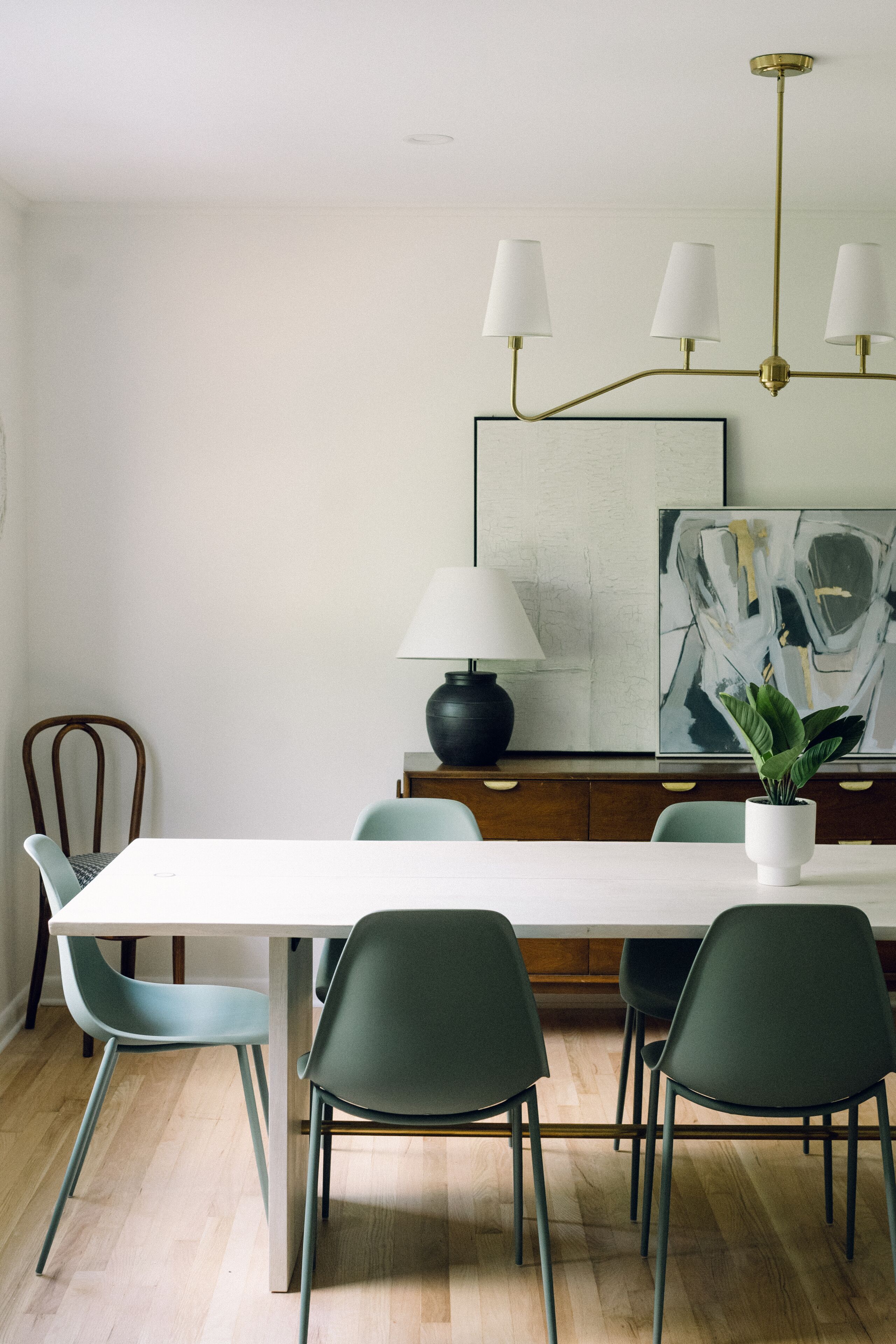 Et spiseområde med et hvidt bord, fire grønne stole, en sort lampe og en moderne lysekrone.