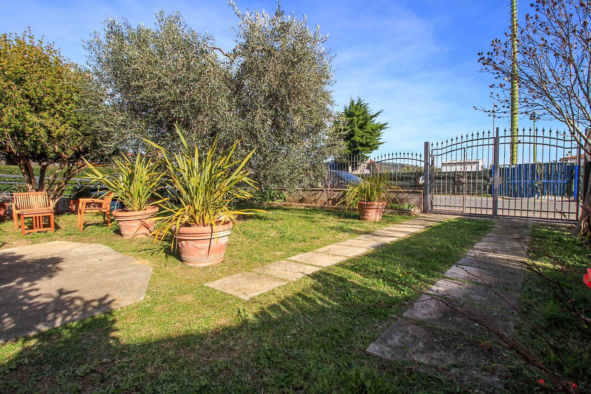 A well-maintained garden with potted plants, a paved walkway, and a metal gate.
